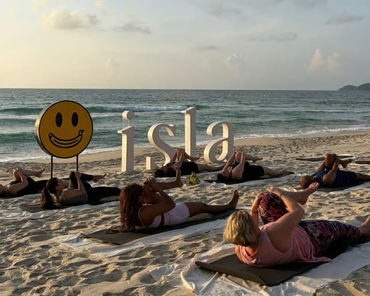 The sunrise class on mats on the sand at Banana Fan Sea Resort, Chaweng Beach, beside the Isla letters and the resort's smiling sign